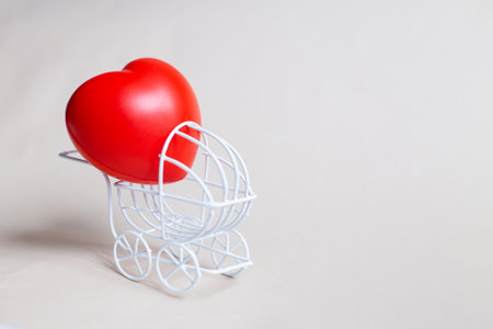 Red heart in the pram or carriage isolated on beige background. Symbol of childbirth. Valentine's Day or newborn greeting cardの写真素材