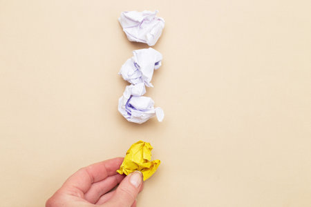 female hand holding crumpled yellow and white paper ib exclamation mark as a concept creative idea and innovation on a beige backgroundの写真素材