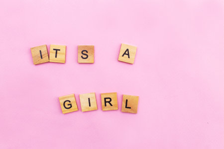 Word Its a girl by wooden cubes on a pink background. Symbol of childbirth, parenthood, birth concept. Invitation festive greeting card on child birthday party.の写真素材