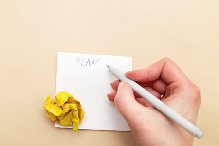 Female woman hand writing a plan or to do list on piece of paper for notes with a crumpled yelllow paper like a bulb as a concept creative idea and innovation on beige backgroundの写真素材