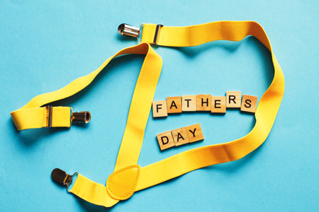 happy father's day lettering made by wooden cubes on a blue background with a yellow suspenders.の写真素材