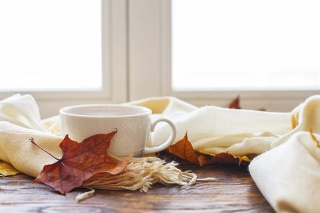 autumn leaves with a cup of tea or coffee next to a scarf on a wooden background with copy space.の写真素材