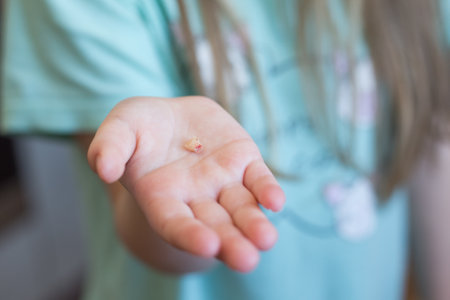 Little girl's hand holding and showing her fallen milk front tooth close up. Milk teeth loss concept