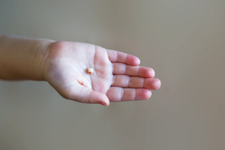 Little girl's hand holding and showing her fallen milk front tooth close up isolated on beige...