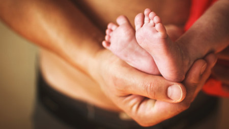 Father holding newborn baby feet with lettle fingers close up on his hands. New family, care, love...