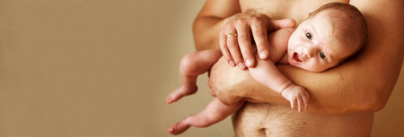 Closeup portrait of young father holding his cute newborn baby with copy space on beige background....