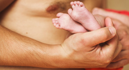 Father holding newborn baby feet with lettle fingers close up on his hands. New family, care, love and baby protection concept.の写真素材