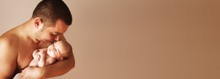 Closeup portrait of young father holding his cute newborn baby and kissing with copy space on beige background. Fathers day holiday, love, care concept.Bannerの写真素材