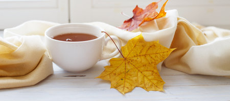 autumn leaves with a cup of tea or coffee next to a scarf on a wooden background with copy space. bannerの写真素材