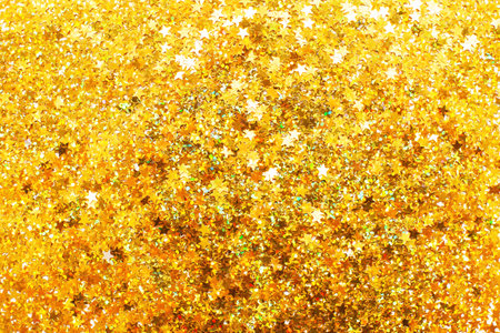 Glittering background of golden sequins in the form of stars closeup. Sparkle christmas festive texture. Confetti on a yellow background. Holiday celebrate, birthday party and anniversary concept.の写真素材