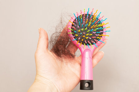 Close up photo of female hand holding lost hair in hand on a grey background with a pink comb. Woman holding her bundle of hair fall with copy space. Healthy nutrition and hair loss problem.の写真素材
