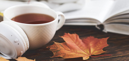 Cup of hot coffee or tea with autumn leaves and headphones on a brown wooden backgroundの写真素材