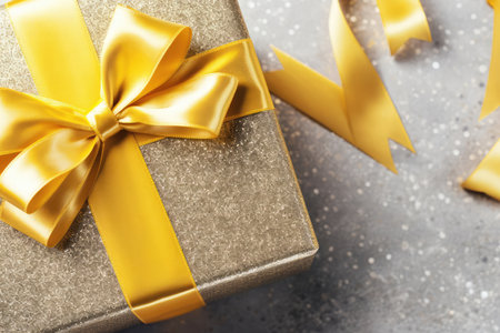 Top view of golden gift box with yellow bow on festive concrete gray background with copy space. Fathers, Christmas, Valentines day, Birthday, anniversary present concept. Holiday saleの素材