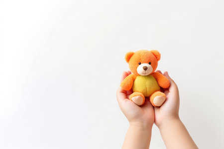 Child hands holding smiling cute little teddy bear on white background with copy space. Kids best friend.の素材