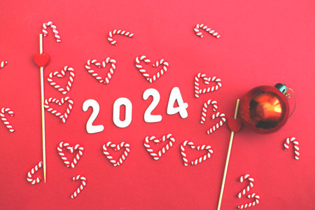 Top view of wooden number 2024 on christmas red background with festive decorations of candy canes and tree toy ball. Christmas greeting card, New Year, winter holidays sale and festive mood concept.の写真素材