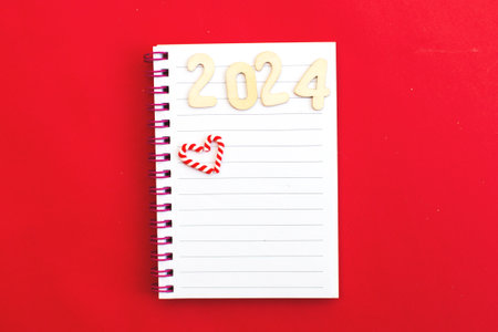 Top view of white paper blank notebook for writing wish list and planning goals, tasks and target for 2024 new year writing to do list on red background.の写真素材