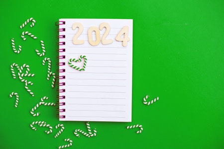 Top view of white paper blank notebook for writing wish list and planning goals, tasks and target for 2024 new year writing to do list on green background.の写真素材