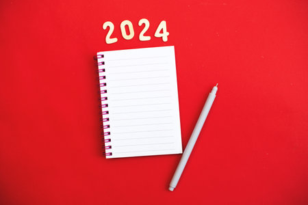 Top view of white paper blank notebook for writing wish list and planning goals, tasks and target for 2024 new year writing to do list on red background.の写真素材