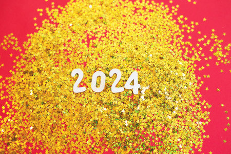 wooden number 2024 on christmas shiny golden background with sparkle festive golden confetti in the form of stars. Christmas greeting card, New Year, winter holidays sale and festive mood concept.の写真素材