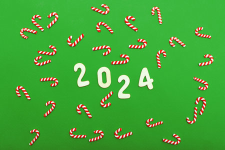 Top view of wooden numbers 2024 on green background with festive decorations of red candy cane. Christmas greeting card, New Year, winter holidays sale and festive mood concept.の写真素材