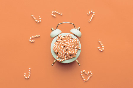 Christmas background with candy canes with the alarm clock on Peach Fuzz background. Color of the...