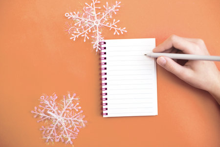 Child hand with pen on white paper blank notebook with winter snowflakes and writing wish list planning tasks for new year writing to do list on Peach Fuzz background. Color of the year 2024の写真素材