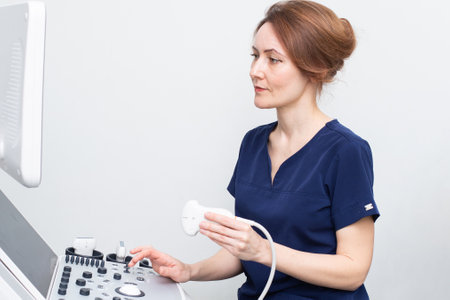 Female doctor woman in uniform sitting in office in a hospital with ultrasound diagnostic machine equipment and ready to examine patients and do ultrasound of heart, thyroid gland or abdominal cavityの写真素材