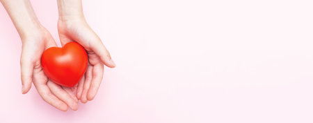 Children's hands holding a red heart as a simbol of care, love, support and protection isolated on a pink background. Kids health care concept. Banner.の写真素材