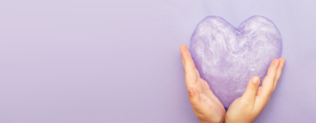 Cute kid little girl playing and making slime at home. Child hands holding slime in the form oh heart on a purple background with copy space. DIY concept.の写真素材