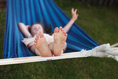 closeup of little girl's feet relaxing in the blue hammock during her summer vacation in the back yardの写真素材