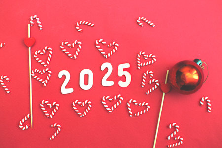 Top view of wooden number 2025 on christmas red background with festive decorations of candy canes and tree toy ball. Christmas greeting card, New Year, winter holidays sale and festive mood concept.の写真素材