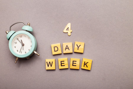 Top view of the inscription four day week making by wooden cubes on grey background with alarm clock. 4 day week business concept of productivity job.の写真素材