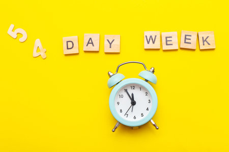 Top view of the inscription four day week making by wooden cubes on yellow background with alarm clock. 4 day week business concept of productivity job.の写真素材