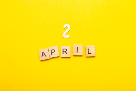 2 April calendar date made by wooden cubes on yellow color background. Calendar, spring concept.の写真素材