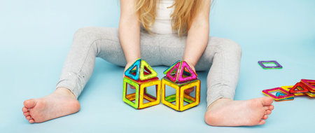 Little girl playing with colorful magnetic constructor toy on a studio blue background. child built a house. Education, development and childhood concept. Banner.の写真素材