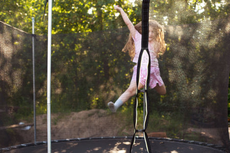Child girl jumping on big trampoline outdoors. Happy smiling kid playing on summer vacation.の写真素材