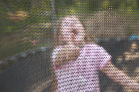 Portrait of a happy smiling excited child girl sitting on trampoline outdoor and showing thumb up...
