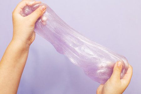 Cute kid little girl playing and making slime at home. Child hands holding and stretching slime on a purple background with copy space. DIY concept.の写真素材