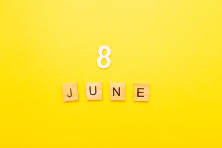 Top view of word 8 June calendar date made by wooden cubes on yellow color background