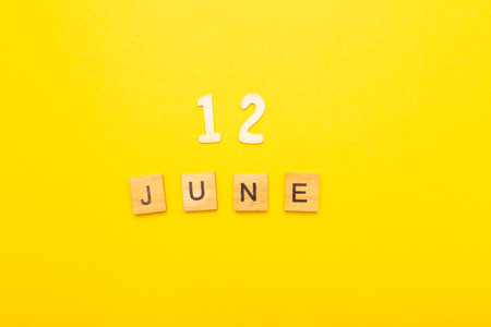 Top view of word 12 June calendar date made by wooden cubes on yellow color background. Calendar and summer concept.の写真素材