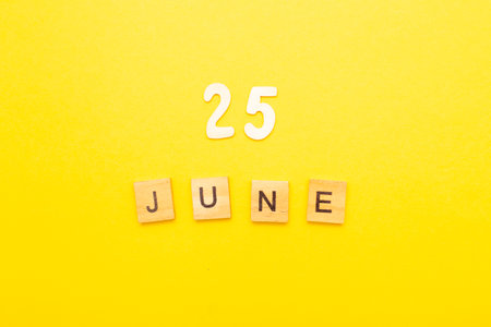 Top view of word 25 June calendar date made by wooden cubes on yellow color background. Calendar and summer concept.の写真素材