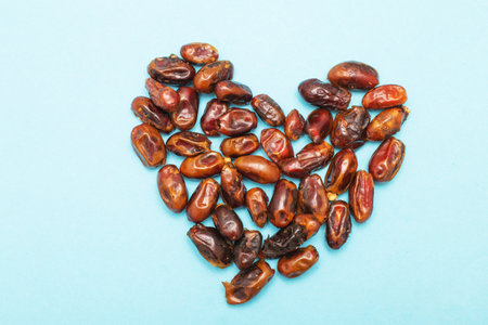 Dried dates creating a heart shape on a light blue surface, healthy food conceptの写真素材