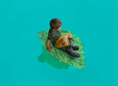 the boy is sitting on a big green sheet. Swims on the blue lakeの写真素材