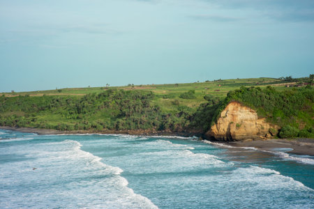 panorama of the scenic view of the beach from a green cliff with very large sea waves. at santolo beach, west java, indonesiaの写真素材