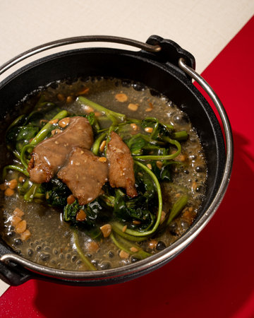 sauteed kale served on a hotplate with pieces of meat and garlic
