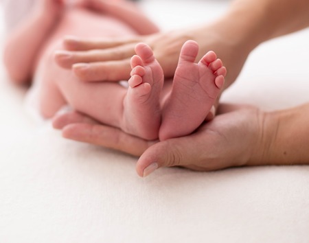 Baby feet cupped into mothers hands. Gentle blurred background of the feet and heels of a newbornの写真素材