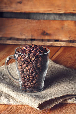 Glass mug with beans on burlap napkin on wooden backgroundの写真素材