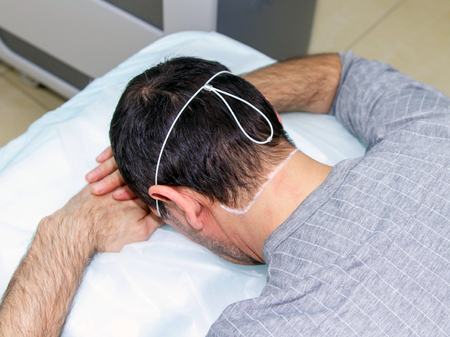 A man is lying face down, getting ready for the procedure of laser hair removal of the neck in a medical clinicの写真素材