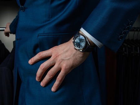 A man in a classic suit with a clock on his hand holds his hand on his belt, closeupの写真素材