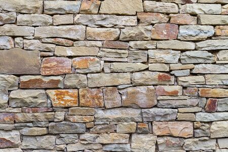 A fragment of stonework from gray and reddish stone in natural light. Stone texture. The wall of a typical building in the mountain auls of the Caucasus on a summer dayの写真素材